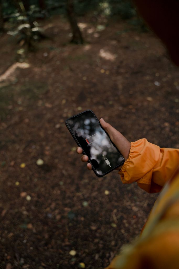 Person in a forest holding a smartphone with a low battery display.