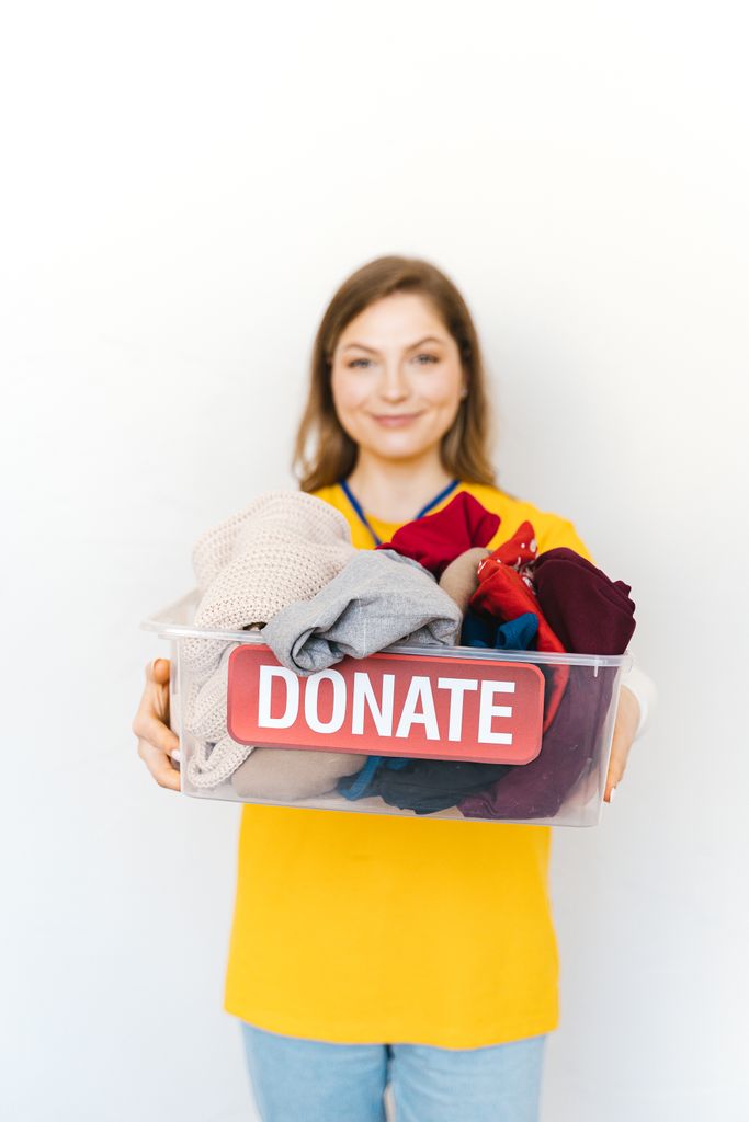 Smiling woman with clothes donation box for charity, emphasizing community support.